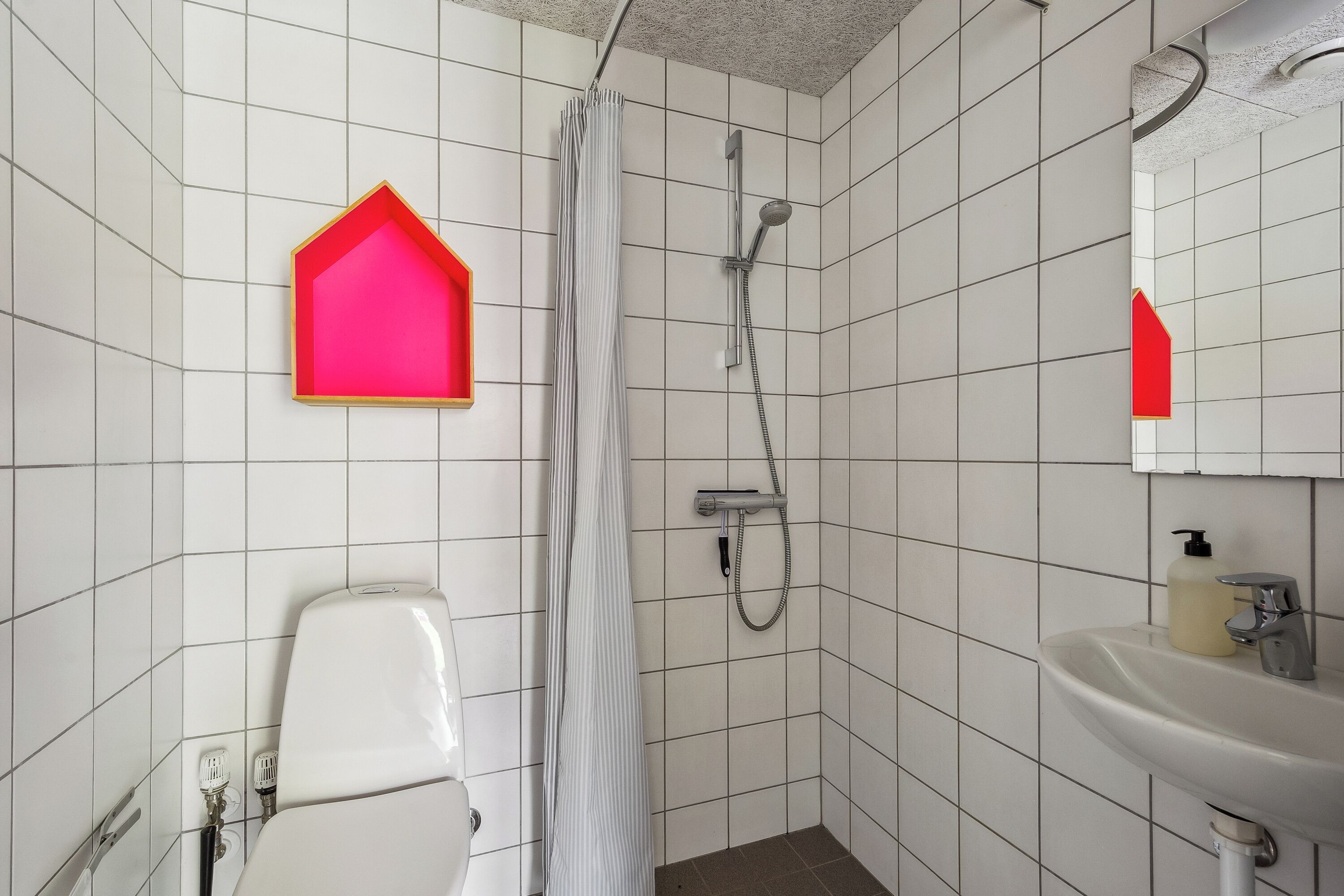 Un baño con paredes de azulejos blancos, ducha, inodoro, lavamanos y espejo.