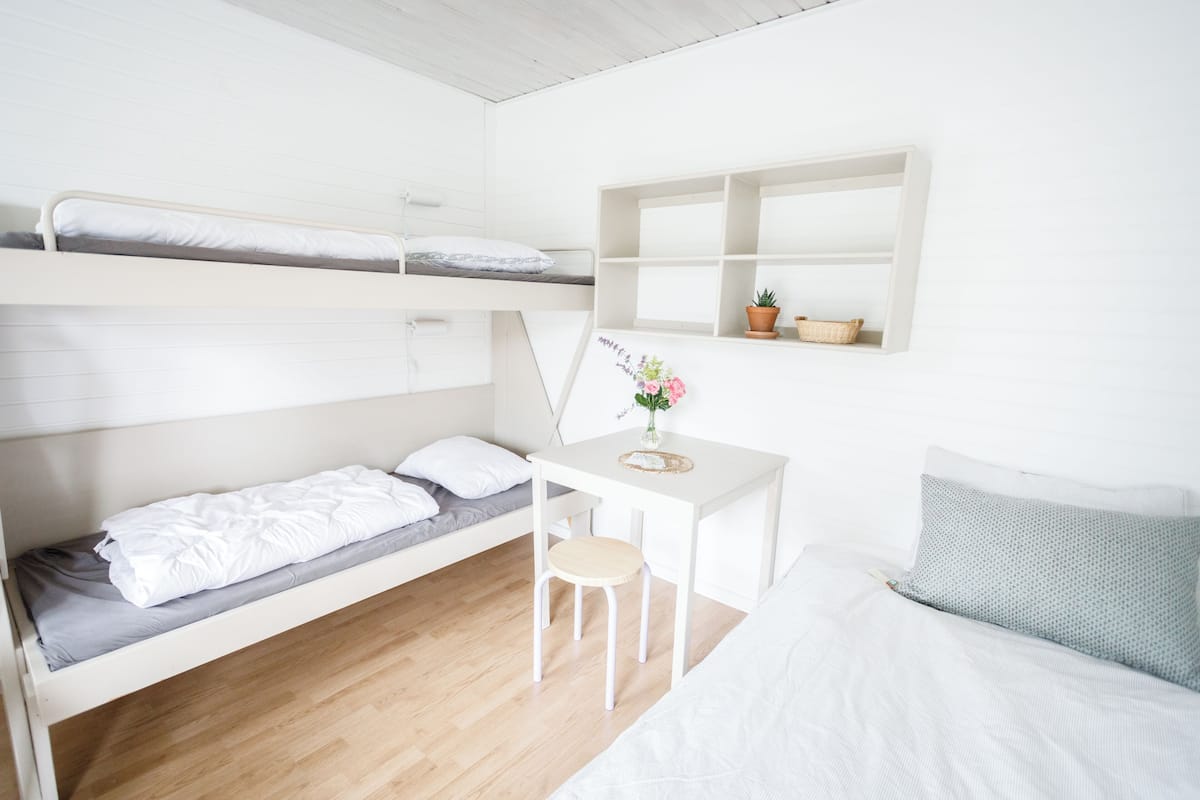 Ett rum i studentkorridorsstil med våningssängar, ett skrivbord, en stol och en liten hylla med växter.