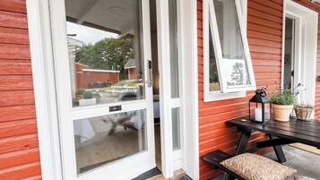 Una casa de madera roja con una puerta corredera de vidrio, una pequeña mesa exterior con cojín y una planta en maceta.
