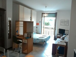 Una habitación compacta con cama, escritorio y silla. Cuenta con un balcón con barandilla y ventana.