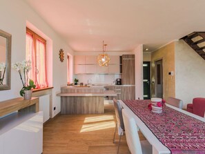 Een moderne keuken met een centraal eiland, houten vloeren en een eethoek met een tafelkleed met dessin.