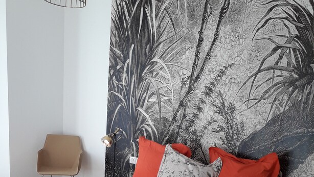 Ein Schlafzimmer mit einem Bett, einem Sessel und einer Wand mit einem Pflanzenmotiv.