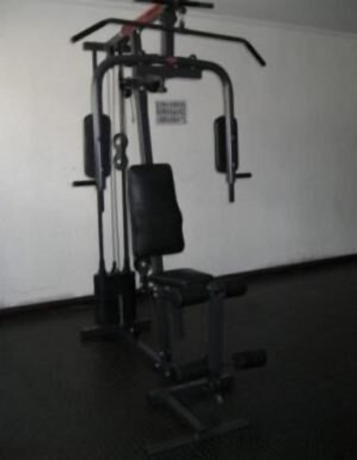 Un gimnasio con una estructura para sentadillas, banco de pesas y discos de pesas.