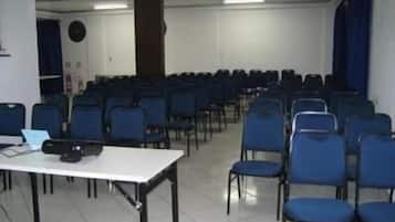 A conference room with rows of blue chairs, a white table with papers, and a clock on the wall.