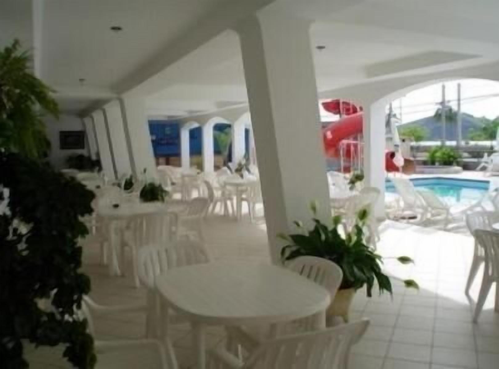 A poolside area with white lounge chairs and tables, a red slide, and a view of the sea.
