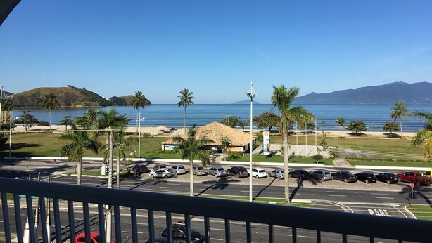 A view of a parking lot with cars, a beach, and a hill in the background.