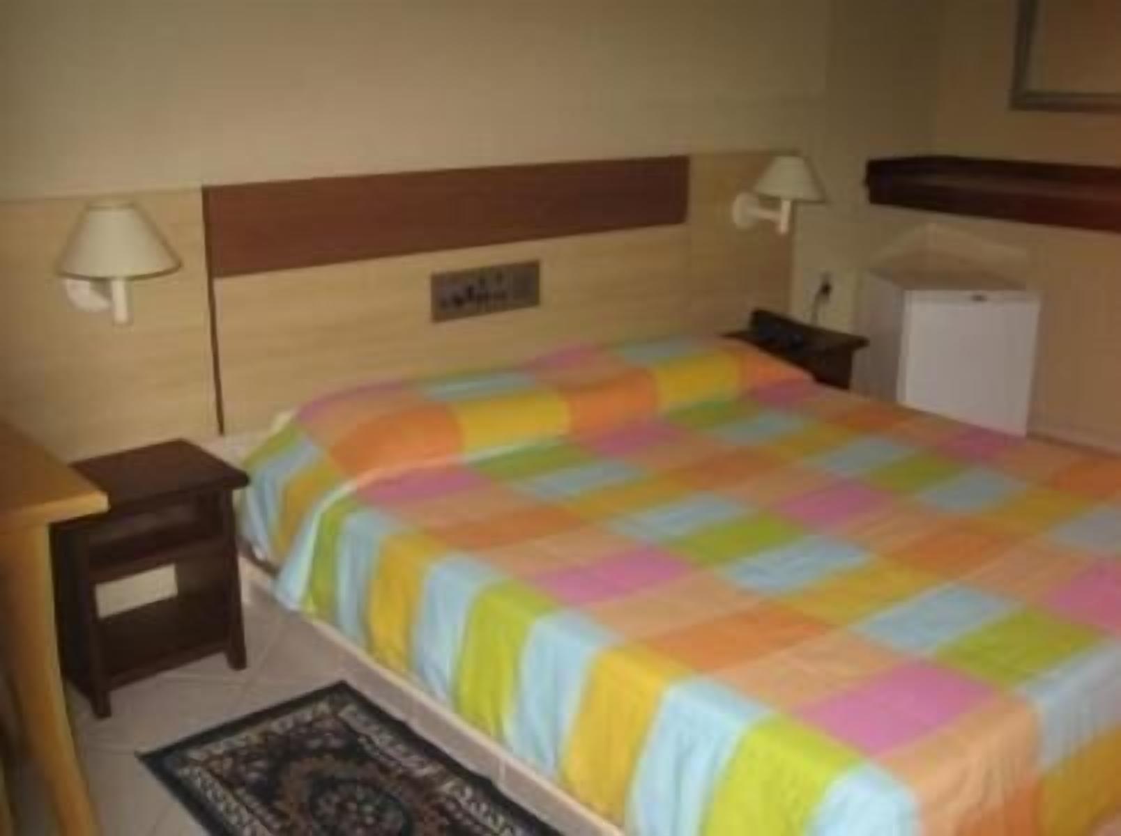 Ein Hotelzimmer mit einem Bett, Nachttischen, einer Lampe, einem kleinen Kühlschrank und einem Teppich.