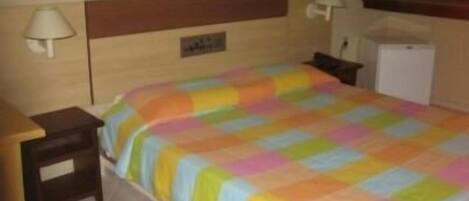 Una habitación de hotel con cama, mesitas de noche, lámpara, refrigerador pequeño y alfombra.