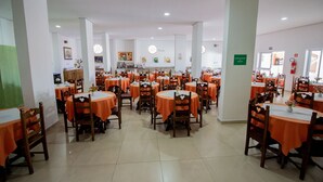 A dining area with round tables covered in orange tablecloths and wooden chairs.