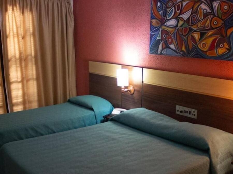 Habitación de hotel con dos camas, cabecero de madera, un cuadro en la pared y una mesita de noche con lámpara.
