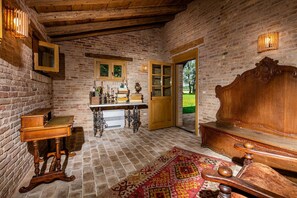 A rustic room with exposed brick walls, a wooden bench, a table with books and decorative items, and a patterned rug. - Agriturismo Casa Gioia (San Michele al Tagliamento)