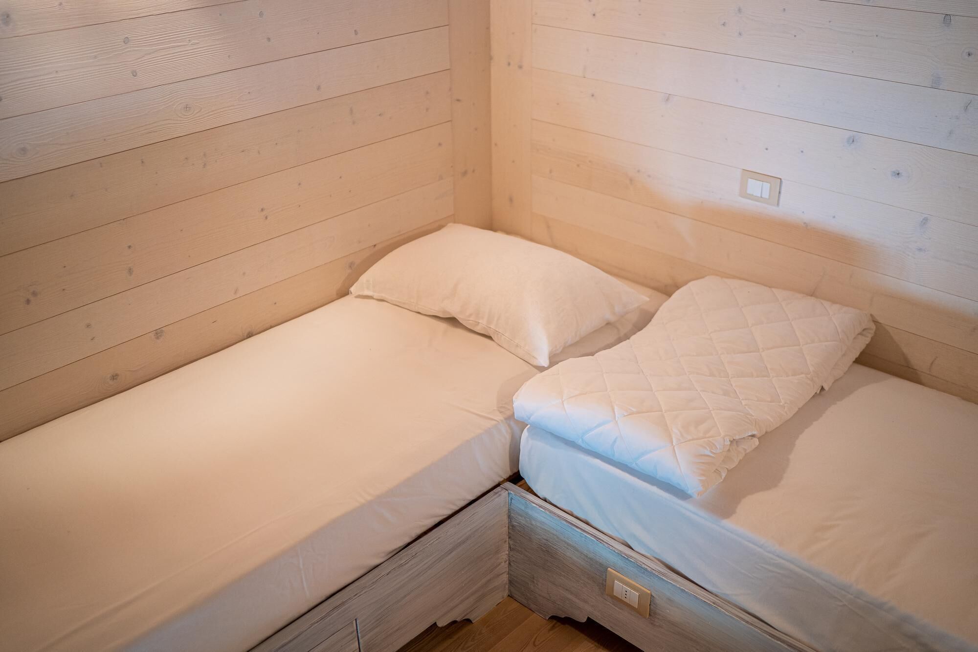 Een kleine kamer met twee bedden, elk voorzien van een wit matras en een gewatteerd dekbed.