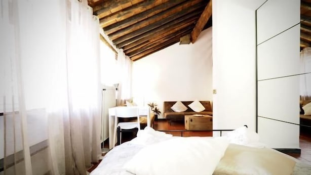 Un dormitorio con techo de madera, una cama con ropa de cama blanca, una mesita de noche y un espejo.