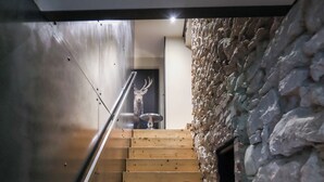 Un escalier en bois, avec un mur en pierre d’un côté et une rambarde en métal de l’autre.