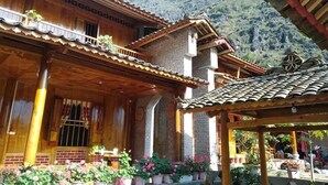 A traditional wooden building with a balcony, potted plants, and a mountain backdrop. - Homestay A San - Hostel (Meo Vac)
