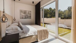Une chambre moderne avec un grand lit, un bureau et une vue sur un jardin, accessible par une porte-fenêtre coulissante.