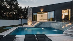 Une maison moderne dotée d’une piscine, d’un espace salon extérieur et d’un escalier menant à une entrée avec porte vitrée.