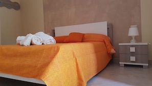 A neatly made bed with an orange bedspread and pillows, a bedside table with a lamp, and a wall-mounted light fixture. - Il Moro della Molpa (Centola)