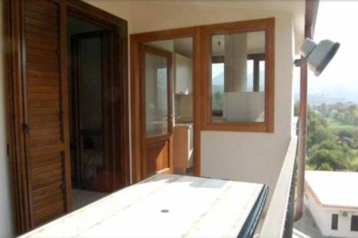 Ein Balkon mit einer Holztür, einem Fenster und Blick ins Grüne.