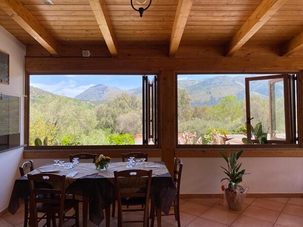 A dining area with a table set for four, large windows with mountain views, and wooden ceiling beams. - Il Moro della Molpa (Centola)