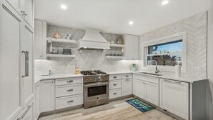 A modern kitchen with white cabinetry, a built-in stove, and a window overlooking a scenic view. - Beachview Retreat: Steps to the beach, Gulf views! (Anna Maria)