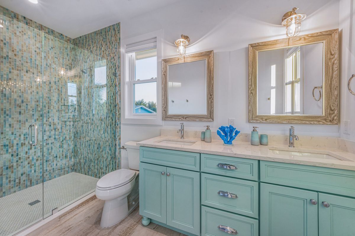 Une salle de bain avec une douche à parois de verre, des toilettes, un lavabo avec un miroir et un meuble-lavabo avec des tiroirs.