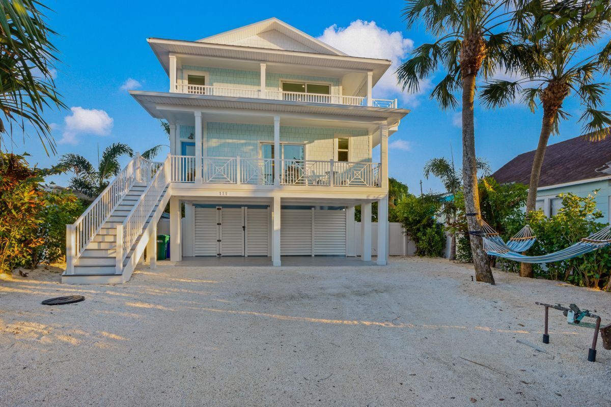 A two-story beachfront house with a balcony, a staircase, and a hammock.