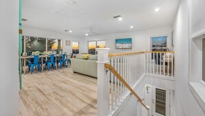A spacious living area with a dining table and chairs, a sofa, and a staircase leading to an upper level. - Beachview Retreat: Steps to the beach, Gulf views! (Anna Maria)
