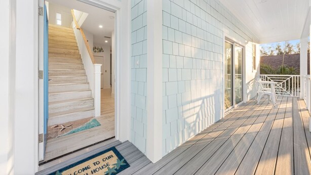 A wooden deck with a white railing, a welcome mat, and a staircase leading to a door. - Beachview Retreat: Steps to the beach, Gulf views! (Anna Maria)