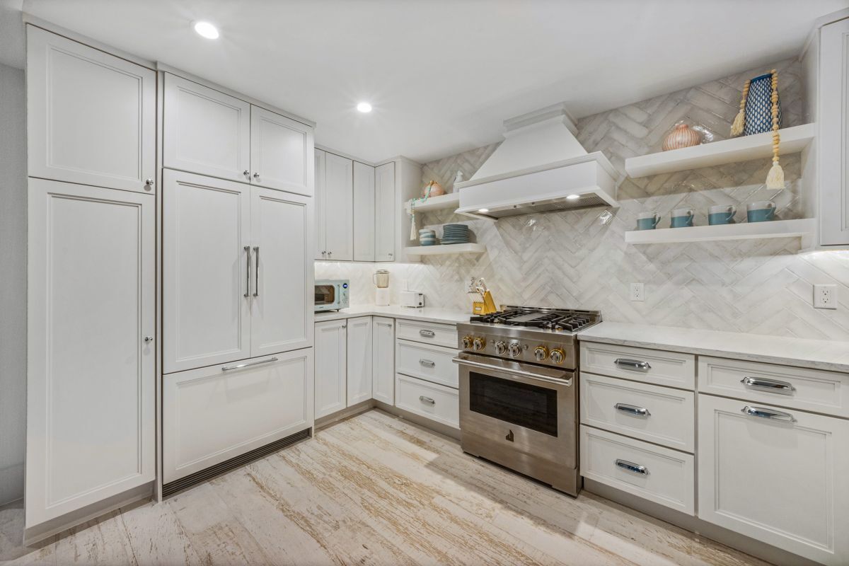 A modern kitchen with white cabinetry, a stainless steel stove, and a herringbone-patterned backsplash.