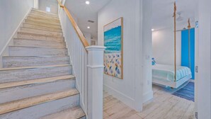 A staircase with white railings and a wooden finish, leading to a bedroom with a bed and a painting of a beach scene. - Beachview Retreat: Steps to the beach, Gulf views! (Anna Maria)