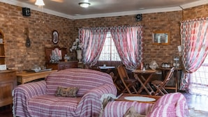 A cozy room with a brick wall, a wooden desk, a cushioned sofa, and a dining table. - Bastille de Blignaut B&B (Edenvale)