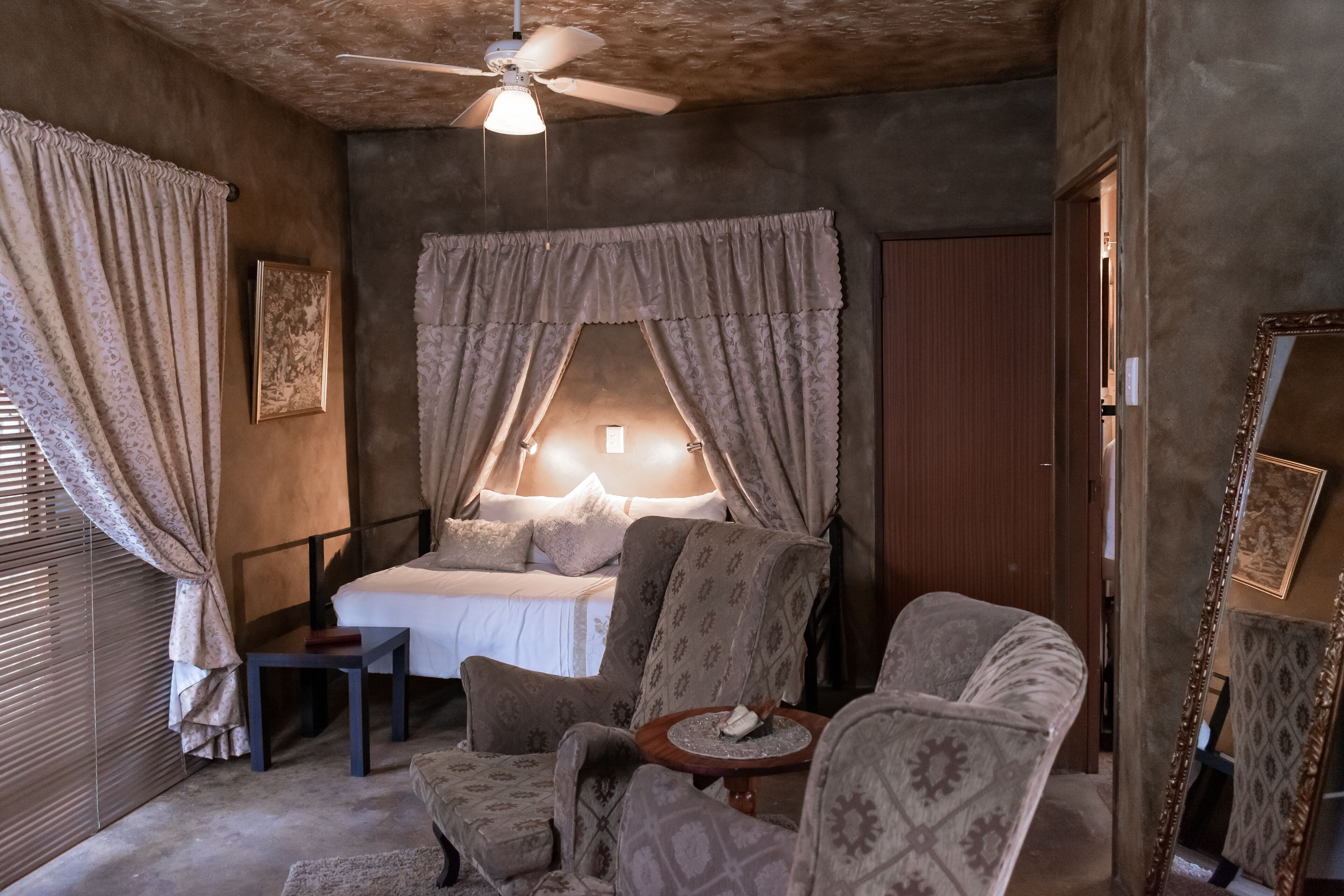 Ein Schlafzimmer mit einem Bett, zwei Sesseln, einem kleinen Tisch und einem Deckenventilator.