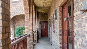 A corridor with brick walls, wooden doors, and a metal railing. - Bastille de Blignaut B&B (Edenvale)
