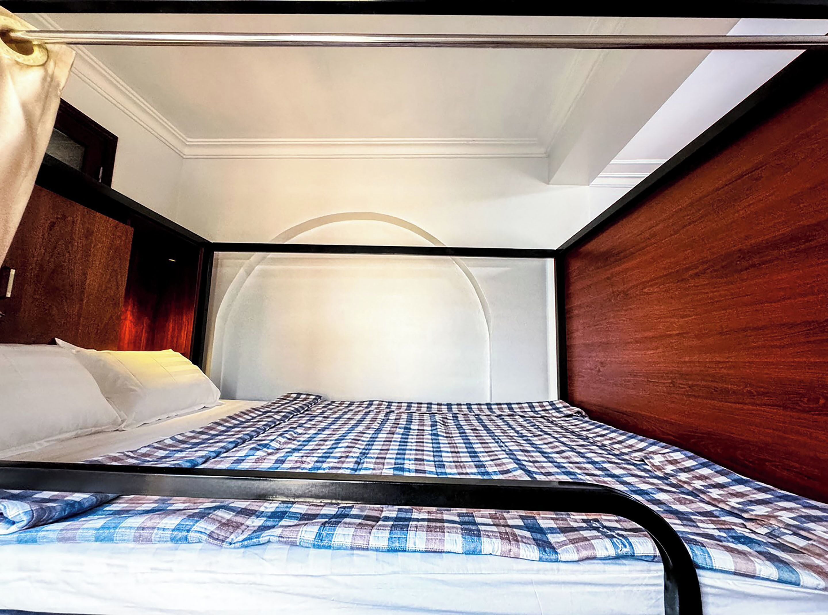 Una habitación compacta con cama individual, colcha a cuadros, cabecera de madera y un diseño sencillo y limpio.
