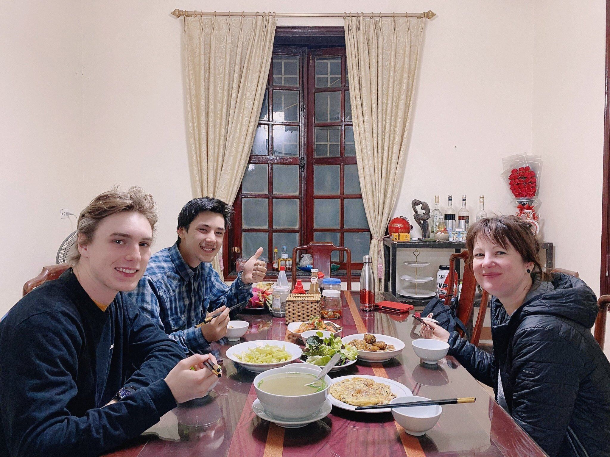 A dining table with various dishes, a window with curtains, and a fan in the background.
