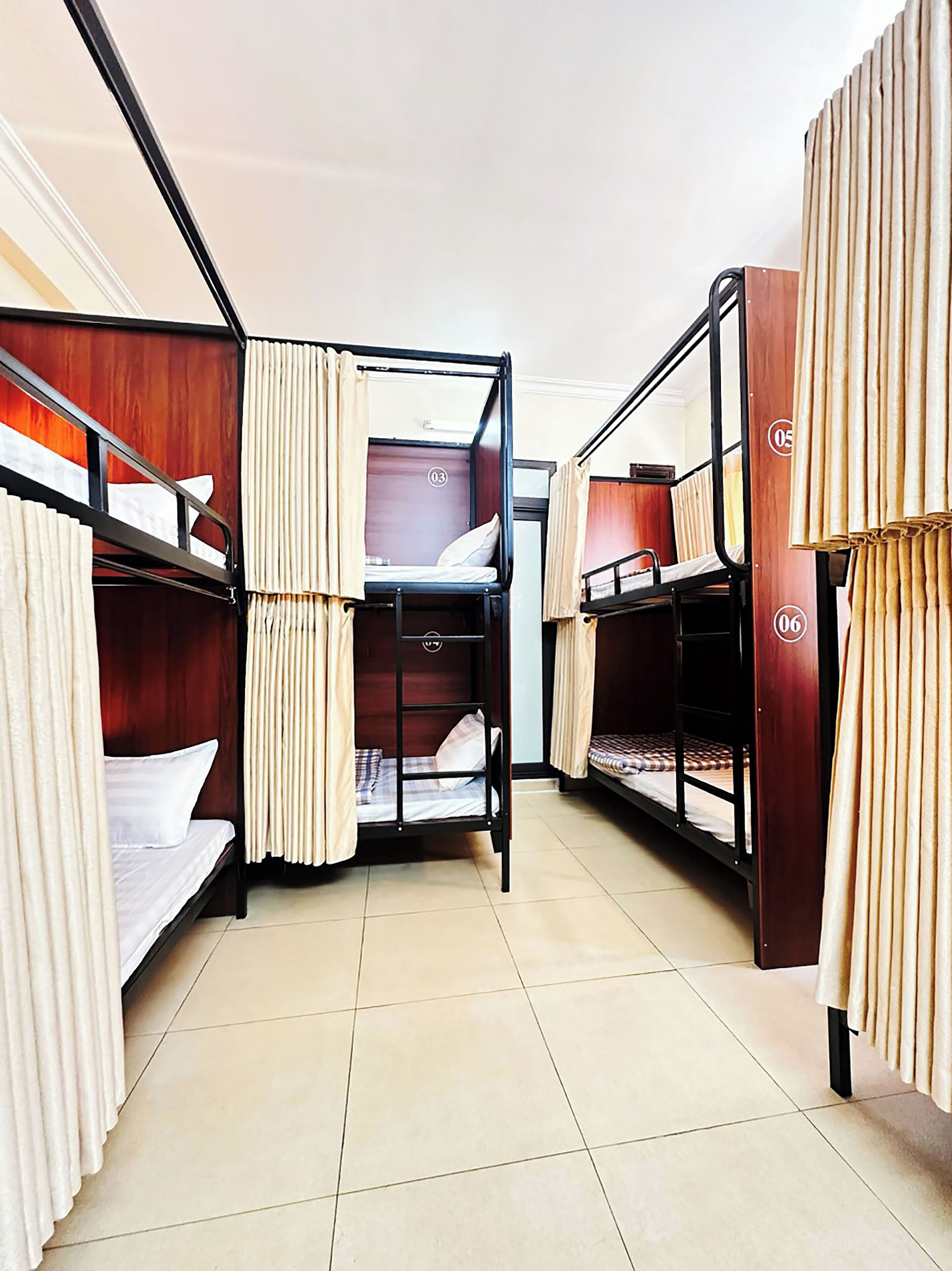 A dormitory room with bunk beds, curtains, and a tiled floor.