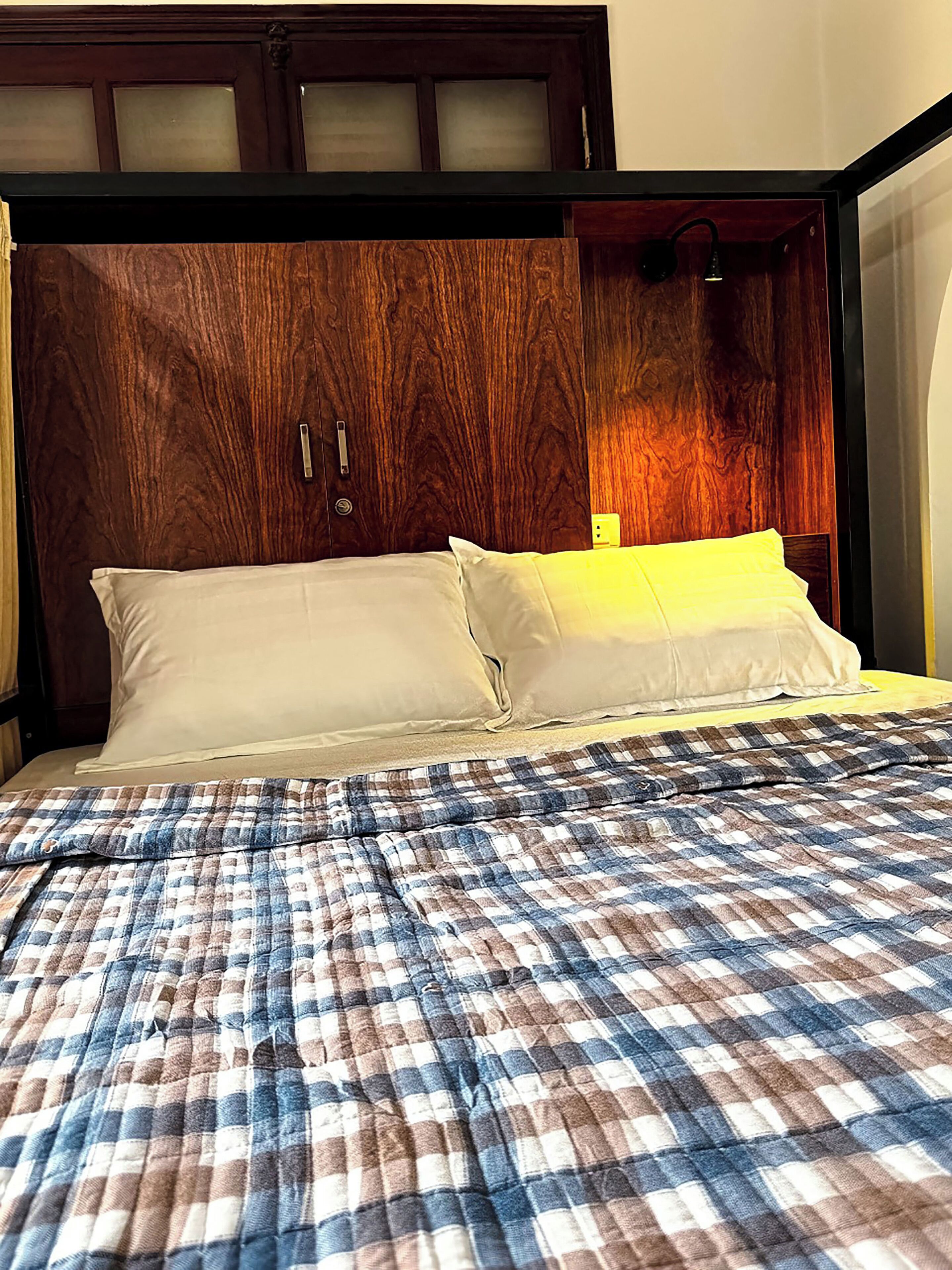 A bed with a plaid bedspread, a wooden headboard with frosted glass panels, and white pillows.