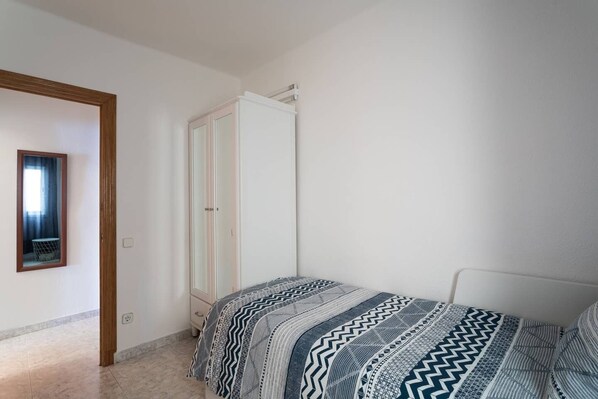 Un dormitorio con cama, armario y espejo en la pared.