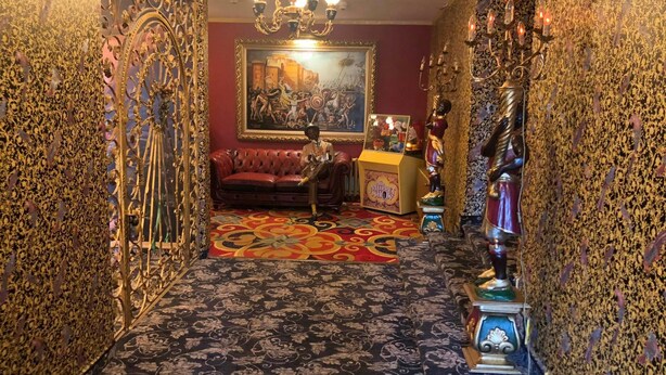 A richly decorated room with ornate gold patterns on the walls, a red sofa, a chandelier, and a painting on the wall. - Hotel Eulenspiegel (Riesa)