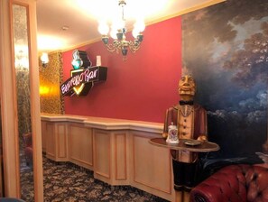 Una zona de bar con un letrero de neón, un candelabro, una estatua y una pared roja.