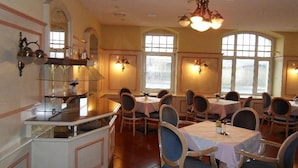A dining area with multiple tables and chairs, large windows, and chandeliers. - Hotel Eulenspiegel (Riesa)