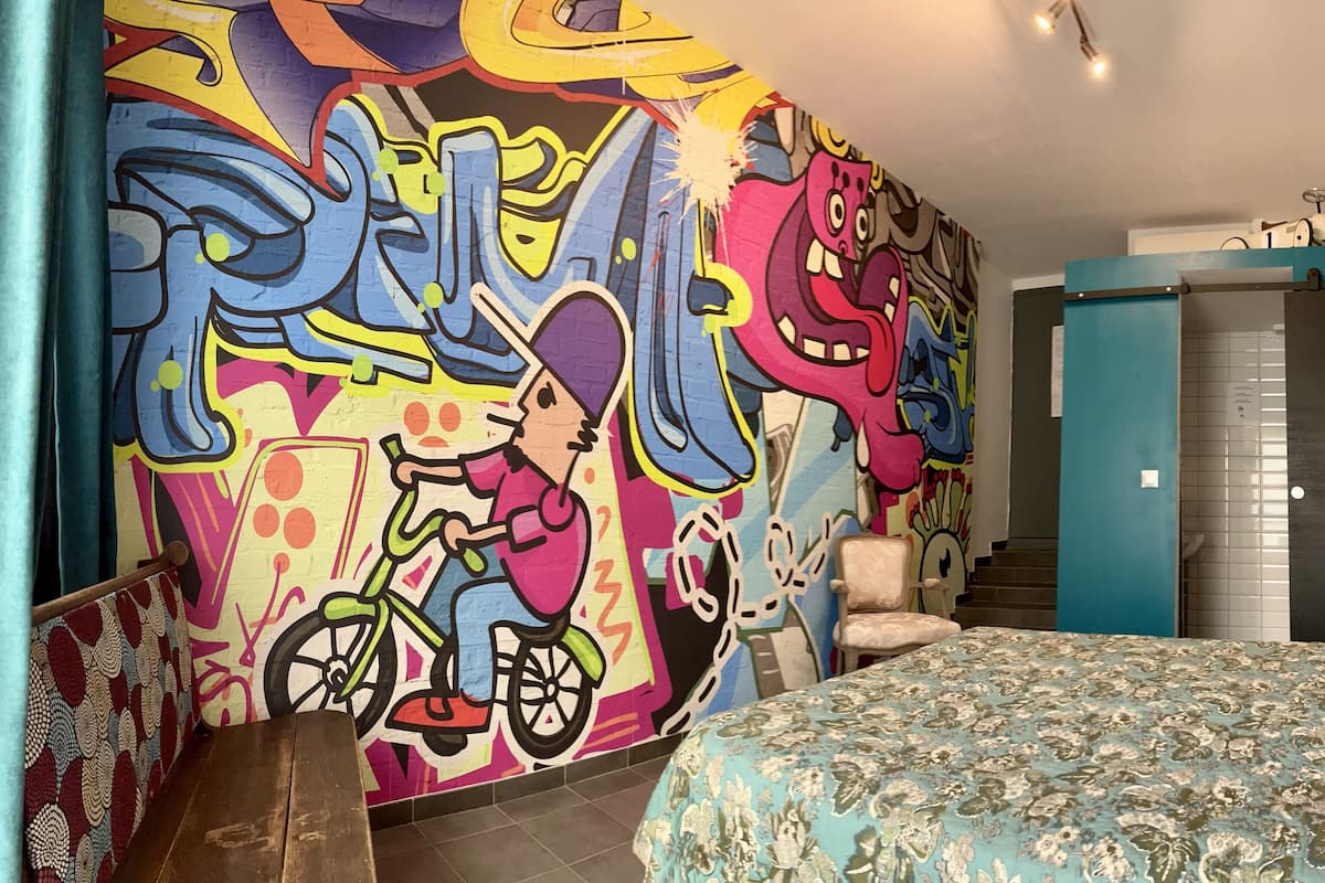 Un dormitorio con un colorido mural de grafitis, una cama con colcha floral y un armario.