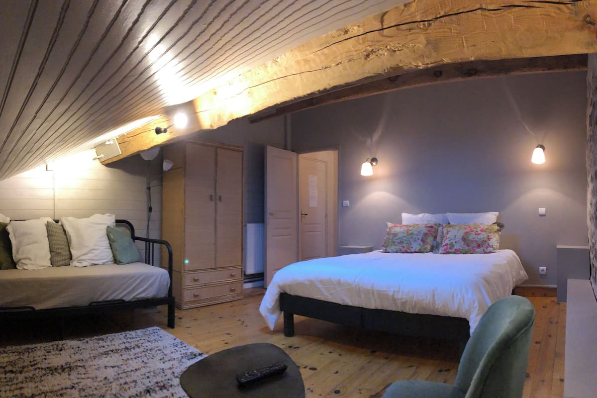 Un dormitorio acogedor en el ático, con techo inclinado, dos camas, un armario y un banco.