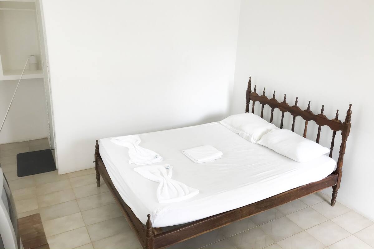 A neatly made bed with white linens and two towels, a wooden headboard, and a tiled floor.