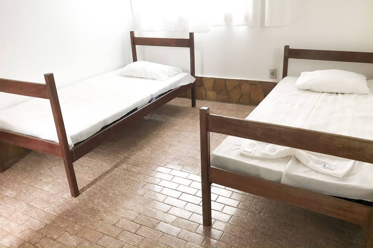A room with three wooden beds, white bedding, and a stone wall.