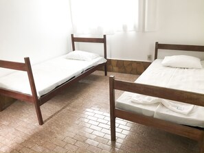 Ein Zimmer mit drei Holzbetten, weißer Bettwäsche und einer Steinwand.