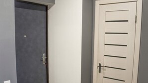 En hall med en grå dörr, en vit dörr och en liten pall.