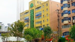 A multi-story building with a green entrance, multiple windows, and flags on flagpoles. - 7Days Inn Chain Hotel (Shanghai Jiangning Road Subway Station Jade Buddha Temple) (Shanghai)