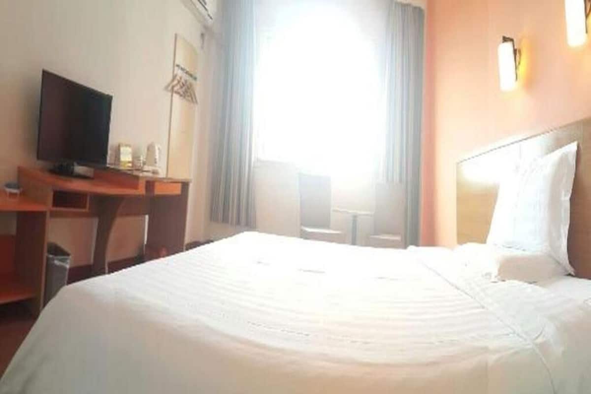 A hotel room with a bed, a desk with a television, and a window with curtains.